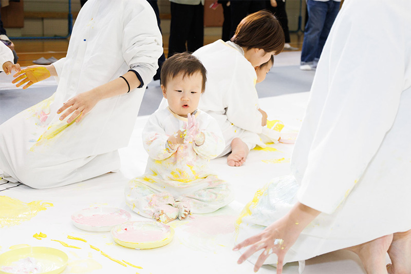 かぞくのおえかくウェアを着用してゆびえのぐで遊んでいる子供の写真