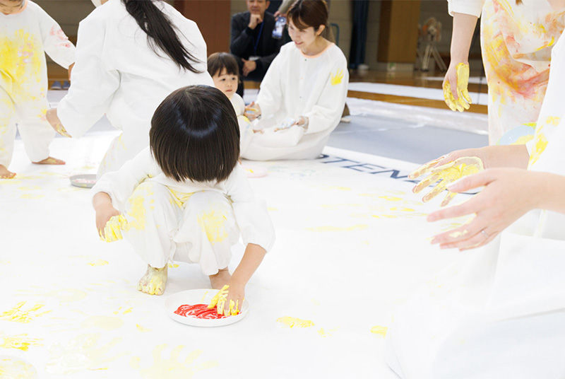 かぞくのおえかくウェアを着用してゆびえのぐで遊んでいる子供の写真
