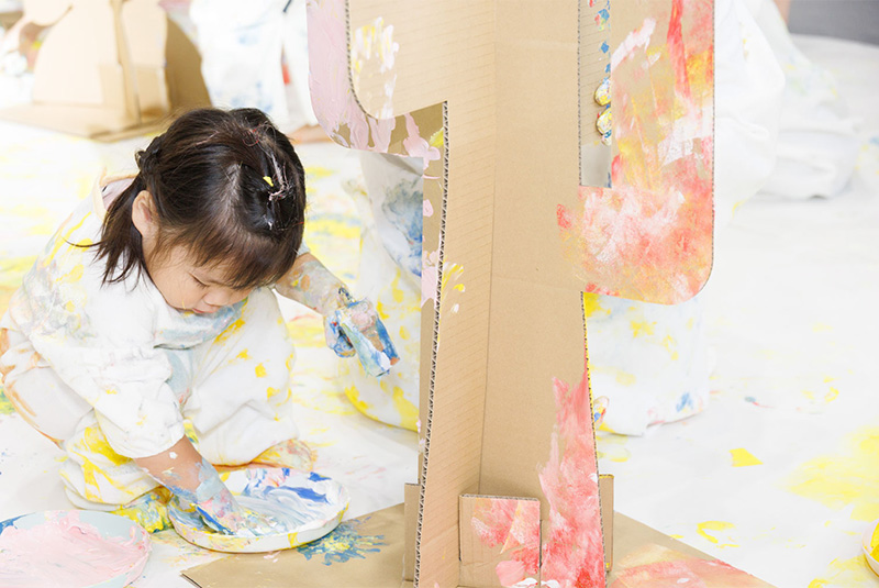 かぞくのおえかくウェアを着用してゆびえのぐで遊んでいる子供の写真