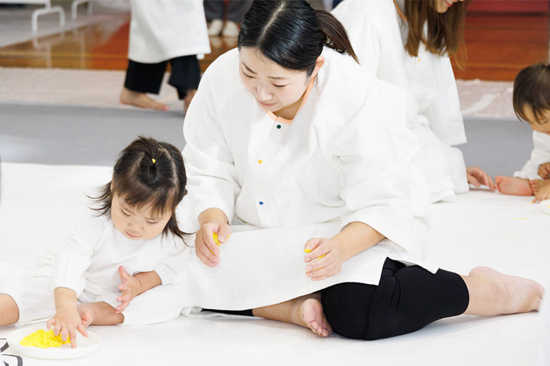 かぞくのおえかきウェアを着用し、ゆびえのぐで遊んでいる親子の写真