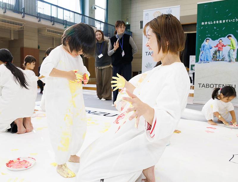 かぞくのおえかきウェアを着用し、ゆびえのぐで遊んでいる親子の写真