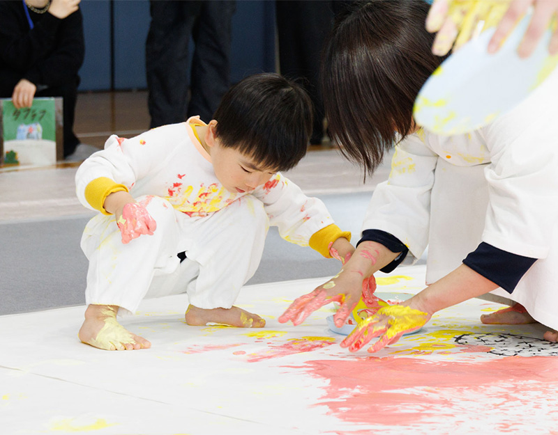 かぞくのおえかきウェアを着用し、ゆびえのぐで遊んでいる親子の写真