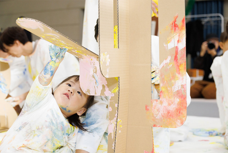 かぞくのおえかきウェアを着用し、ゆびえのぐで遊んでいる親子の写真