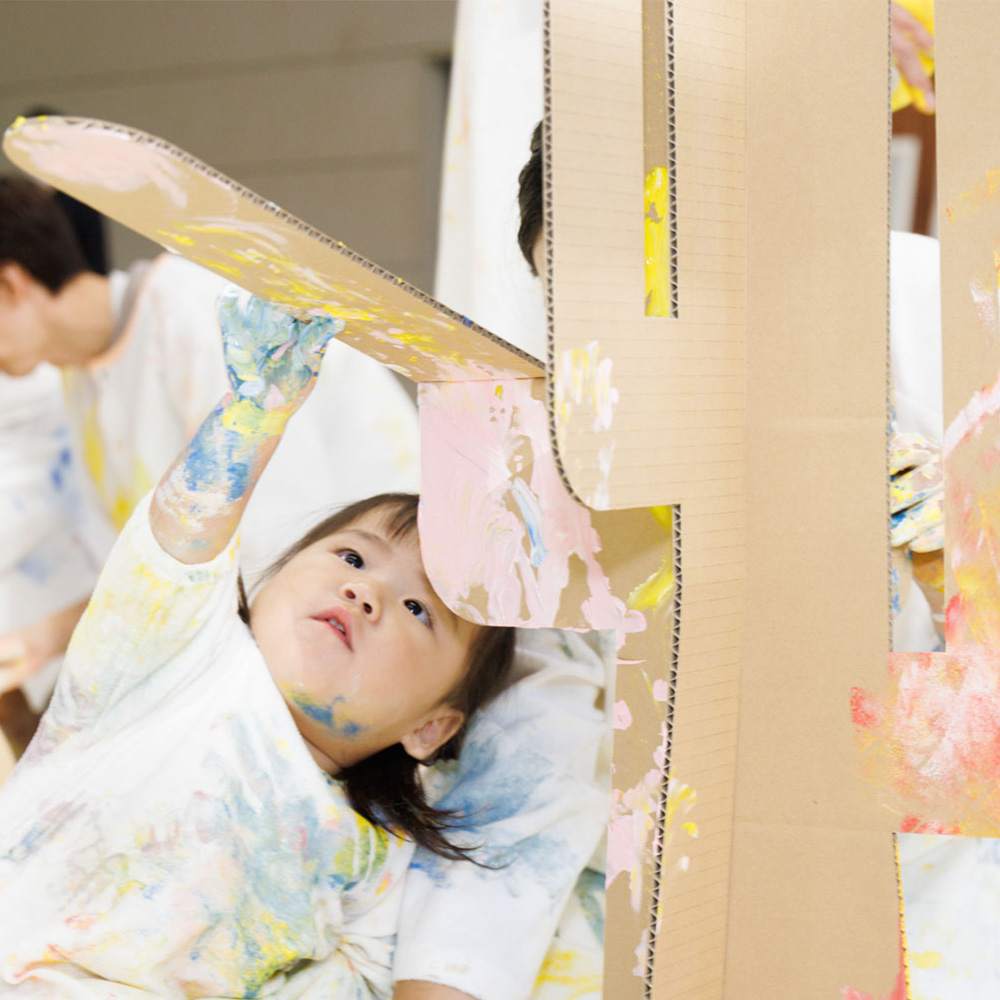 かぞくのおえかきウェアを着用した親子が長い筒を持って遊んでいる写真