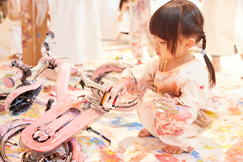 かぞくのおえかきウェアを着てへんしんバイクをゆびえのぐでペイントしている子供達