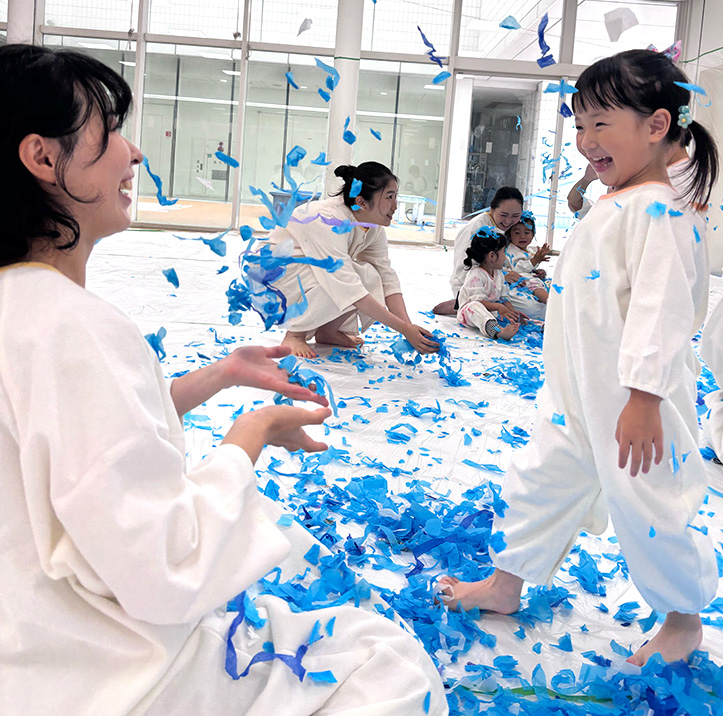 青色の花紙を使って紙吹雪あそびをする親子の写真